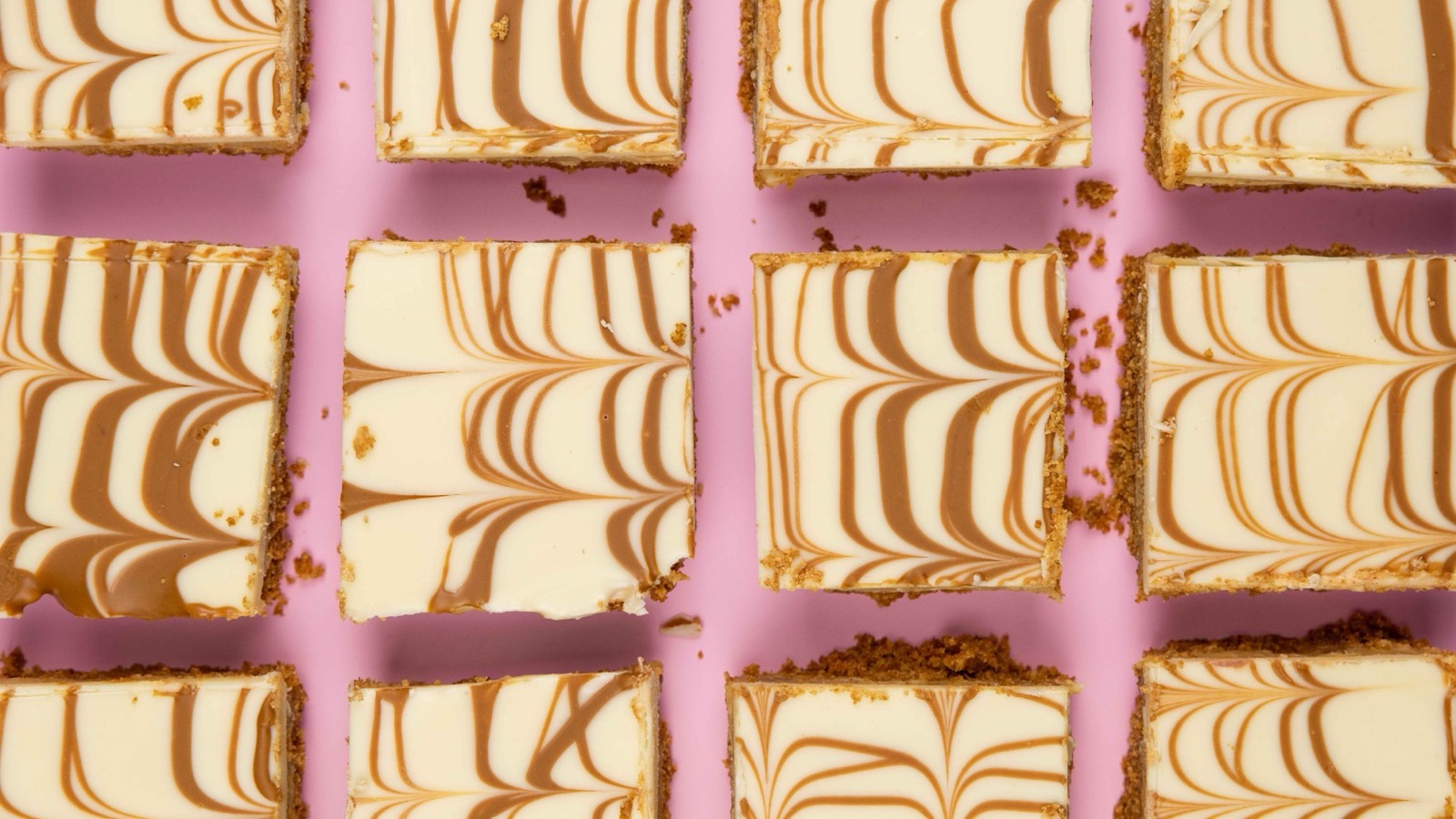 Overhead grid of home-baked Biscoff Brownies with white chocolate topping and caramel swirl, shown on a pink background